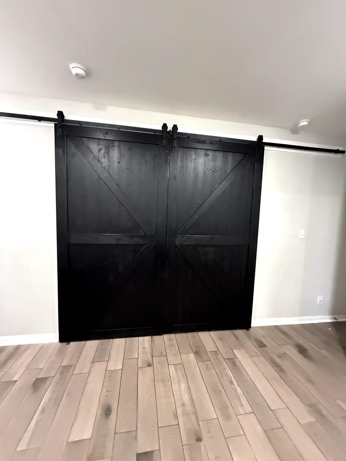 Custom black sliding barn door installed on a hardwood-floored hallway