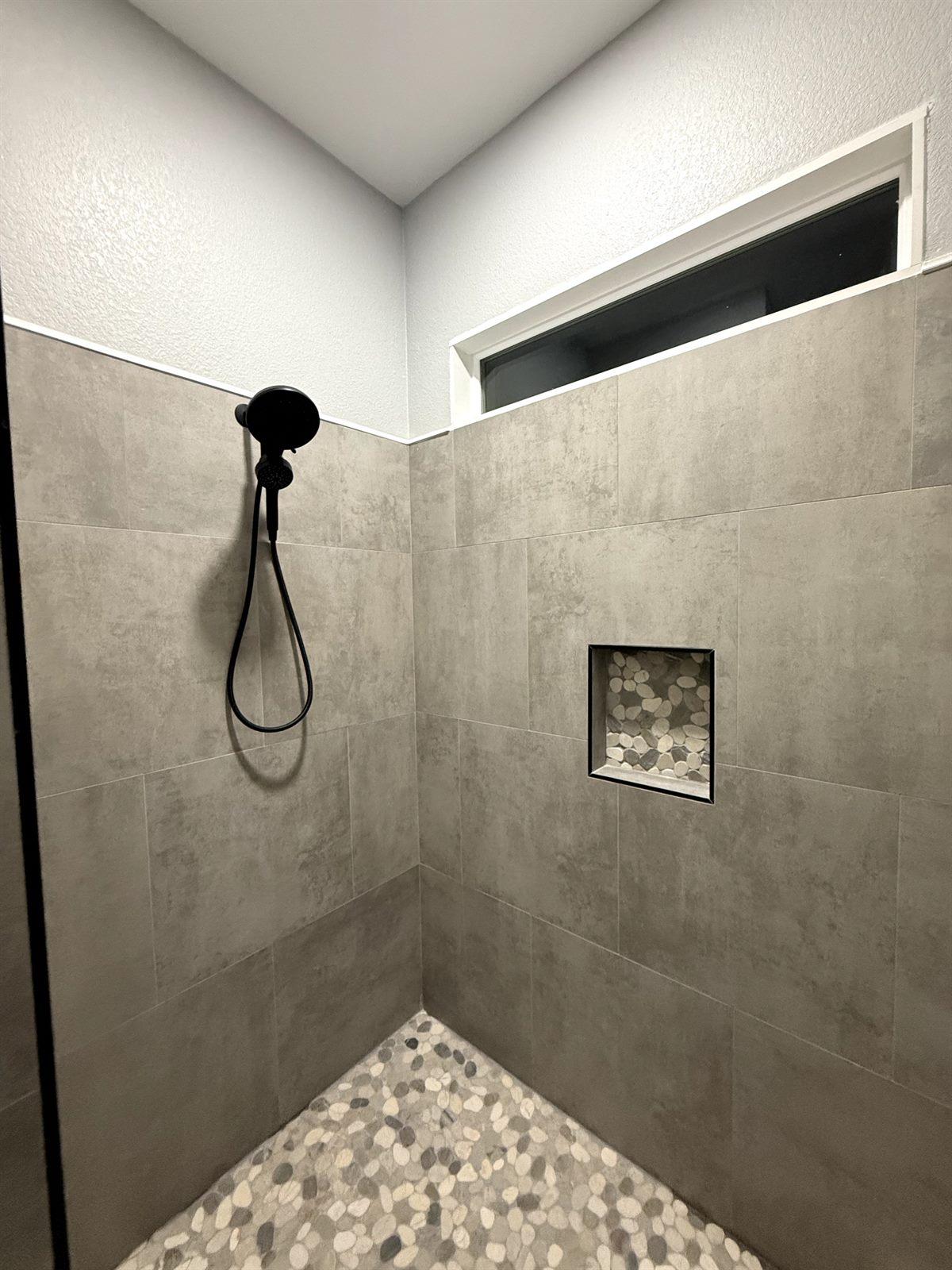 Large-format tile walk-in shower with a pebble floor and matte black shower head